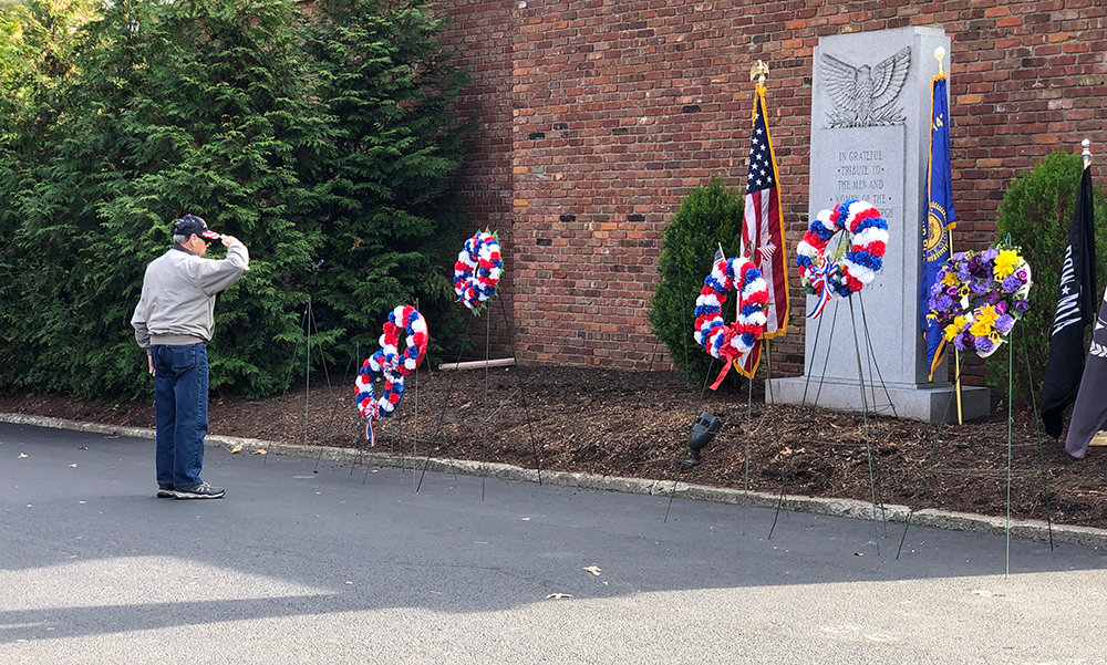 A Newburgh veteran places a wreath on behalf of his military organization in front of the memorial alongside the other wreaths and flags.